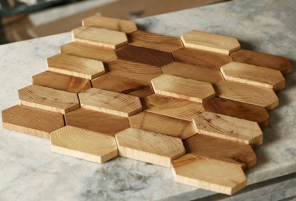 White oak tambour wood tiles in hexagonal and elongated shapes create a honeycomb pattern on a light stone surface. | Custom tambour and architectural wood specialists