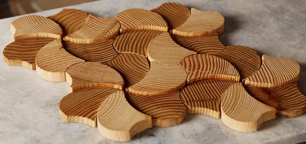 White oak tambour panels with curved, leaf-like shapes and rich grain create a stunning mosaic accent above a stone surface. | Custom tambour and architectural wood specialists